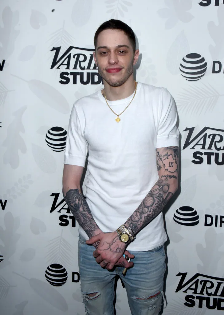 A portrait image of Pete Davidson (Peter Michael Davidson) wearing white T-Shirt standing straight to the camera in a Show Program.